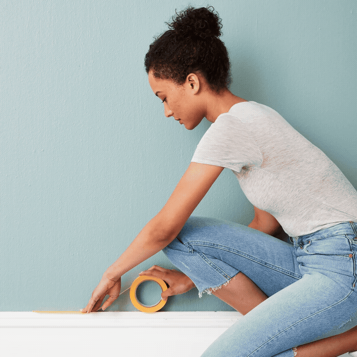 Woman applying Painter's Washii Tape to the baseboard
