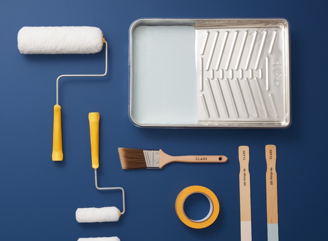 Flat lay of Clare supplies including rollers, brushes, tape, stir sticks and a metal paint tray