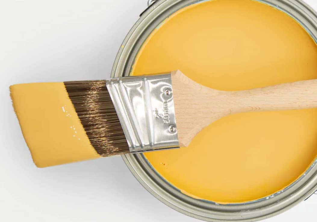 Paint brush dipped in yellow paint resting on open paint can