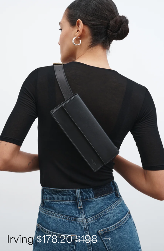 Astrid in a fitted black top and blue jeans wears a sleek black Irving Convertible Clutch diagonally across her back, featuring a compact rectangular silhouette and wide strap.