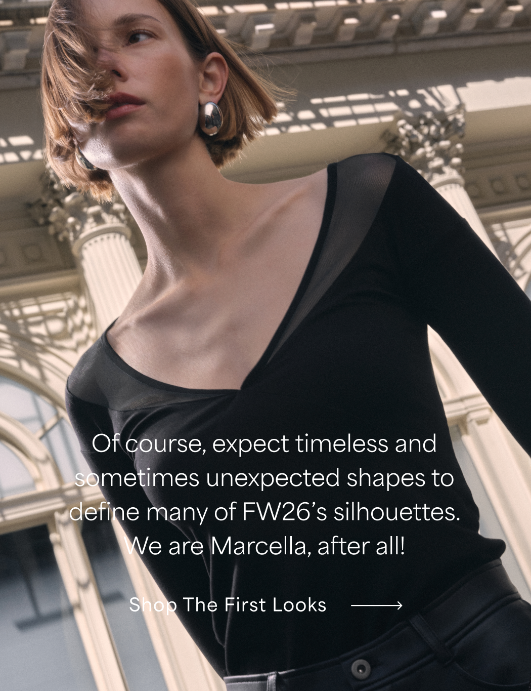 Mali in a black Taylor Top with sheer neckline panels poses against classical architecture, with text reading “Each piece is designed to reflect your own self-assurance, today and for years to come” and “Shop The First Looks.”