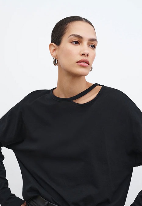 Astrid poses in a relaxed black Jerome Cutout Top featuring an asymmetric cutout detail at the neckline.