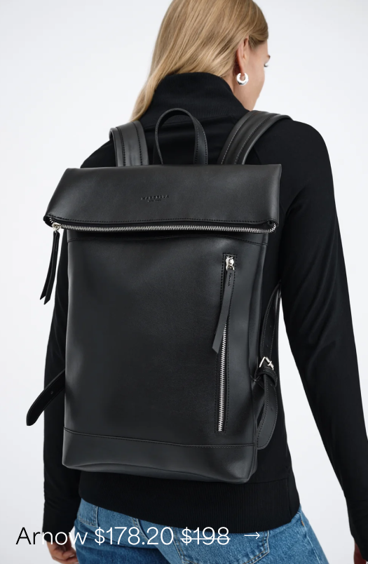 Maritza shown from behind wears a black Arnow Backpack with a fold-over top, shoulder straps, and front zipper details.