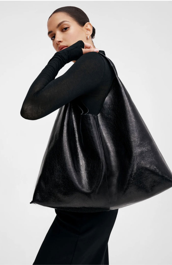 Astrid dressed in black carries an oversized onyx Kelly Tote over her shoulder, shown from the side to highlight the bag’s spacious sculptural silhouette.