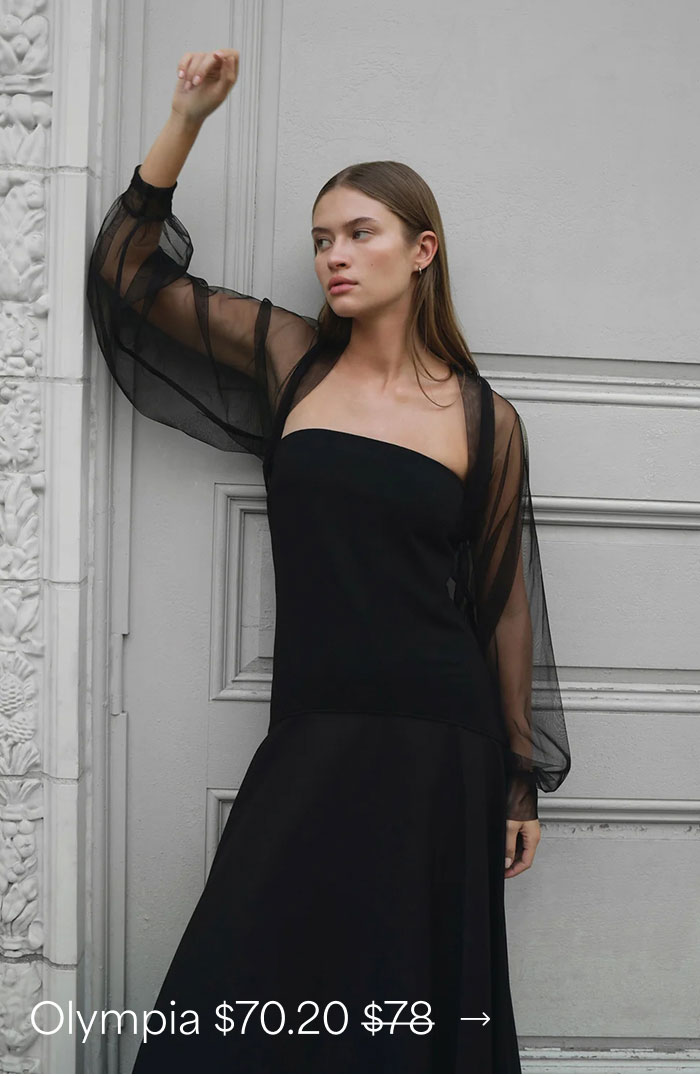 Bianca wears a black mesh Olympia Bolero with voluminous long sleeves over a strapless black dress while posing against an ornate gray wall, priced at $70.20, originally $78.