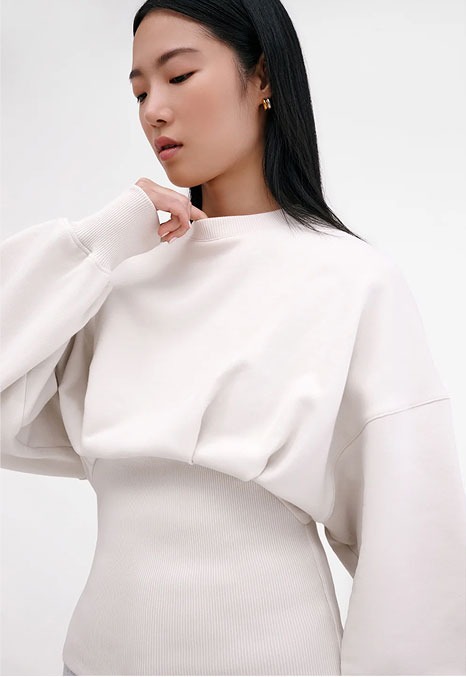 Xun wears a cream Maris Sweatshirt with relaxed sleeves over a fitted ribbed ivory layer.