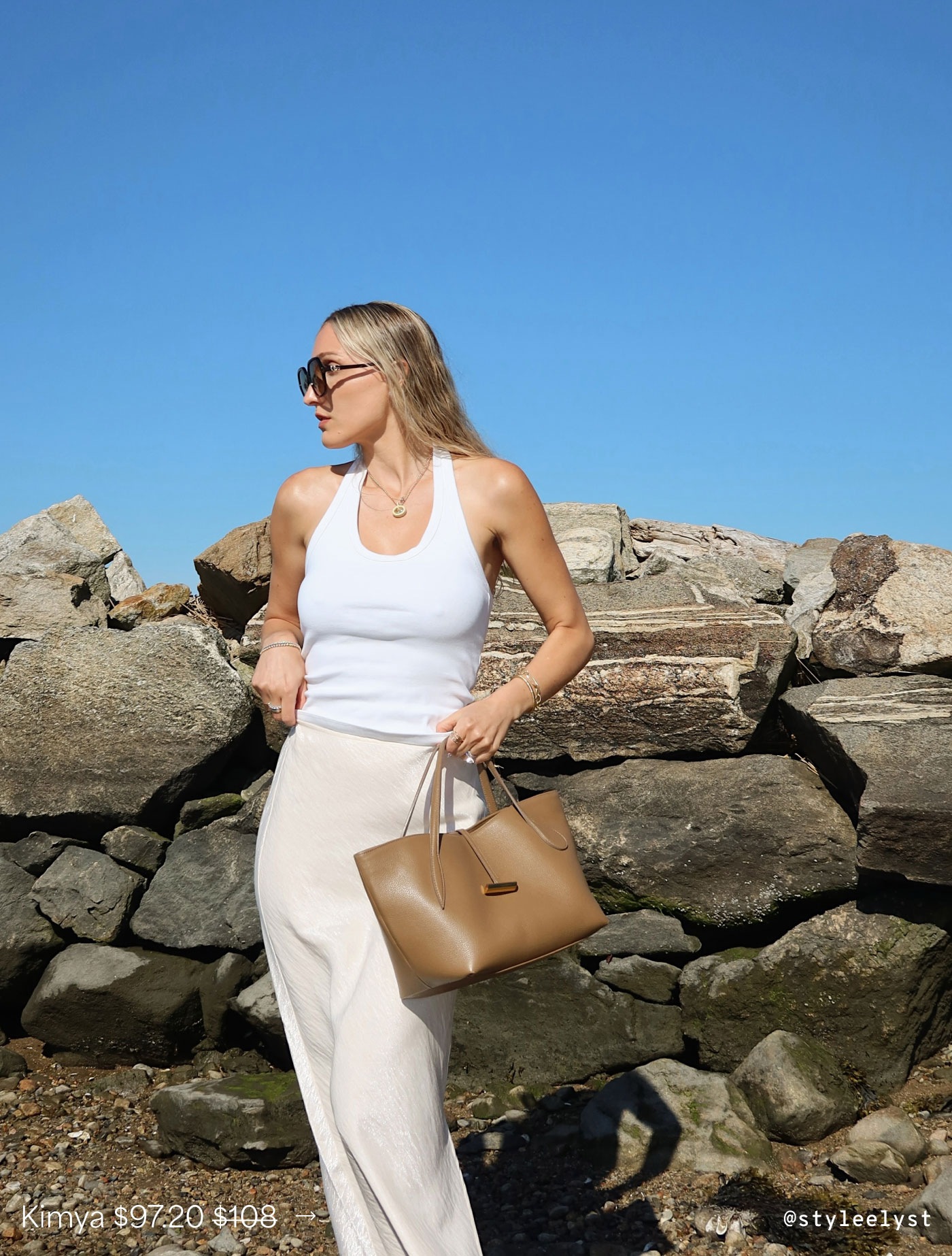 @styleelyst by a rocky shoreline wears a white tank with a pearl Kimya Slip Skirt and carries a tan tote, featuring The Kimya Slip Skirt on sale for $97.20, originally $108.