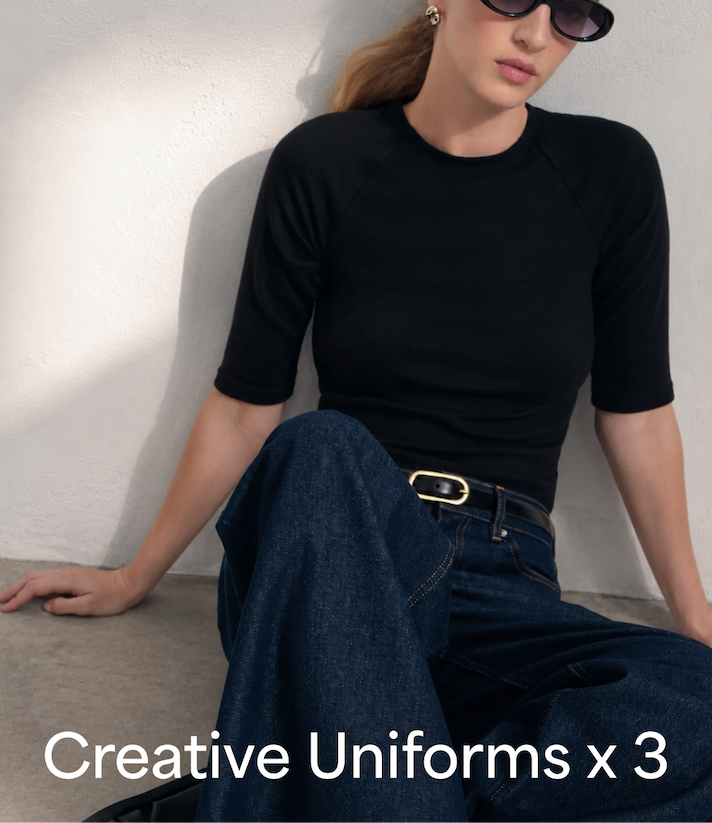 Sophie wearing a black High Rise Top, Linda Jeans in dark blue, and a black Bay Sandals sits against a white wall beneath the overlaid headline “Creative Uniforms x3.”