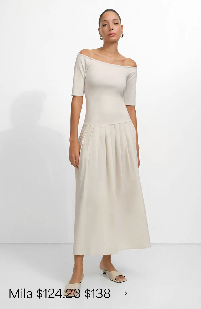 Carmel wears a cream Mila Dress with a pleated skirt and matching heels, priced at $124.20, originally $138.