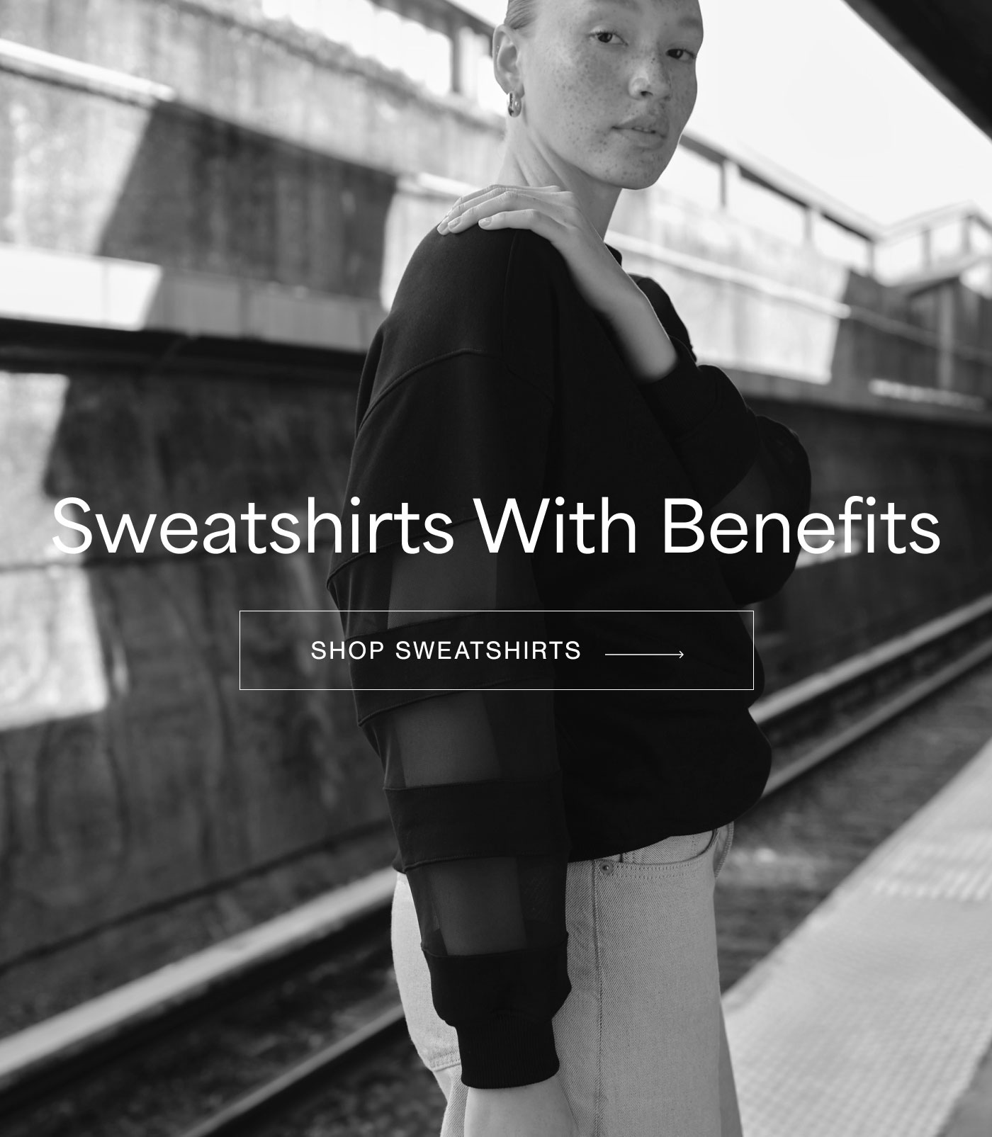 Tehya wears The Beatrix Sweatshirt with sheer mesh panel sleeves and light-wash jeans while posing on a subway platform, with text reading "Sweatshirts With Benefits,” and “SHOP SWEATSHIRTS.”