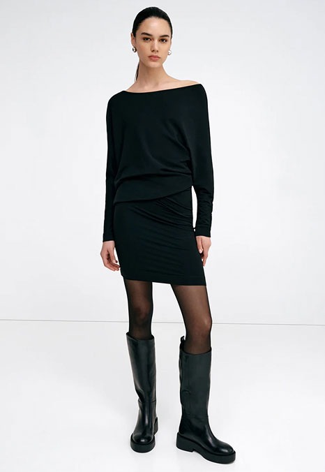 Mily wears a fitted black Beekman Sweatshirt Dress, sheer tights, and knee-high black boots.