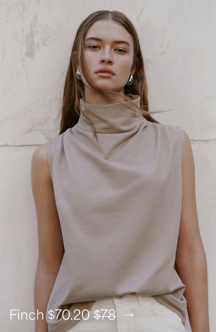 Bianca wears a sand Finch Top with a draped high neckline and light trousers, priced at $70.20, originally $78.
