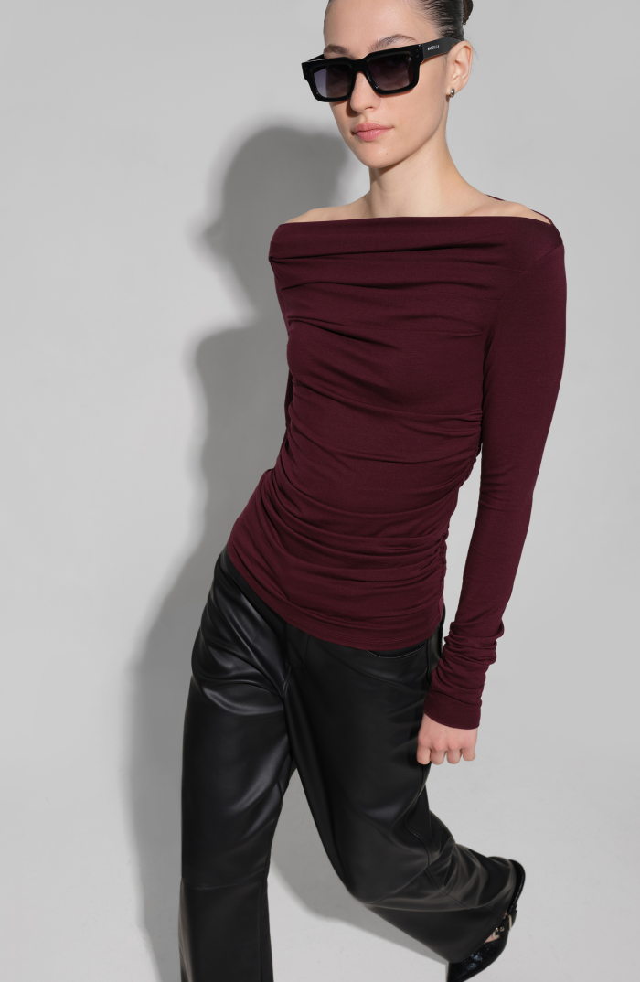 Milana wears a burgundy Cooper Top, black leather pants, and dark glasses.