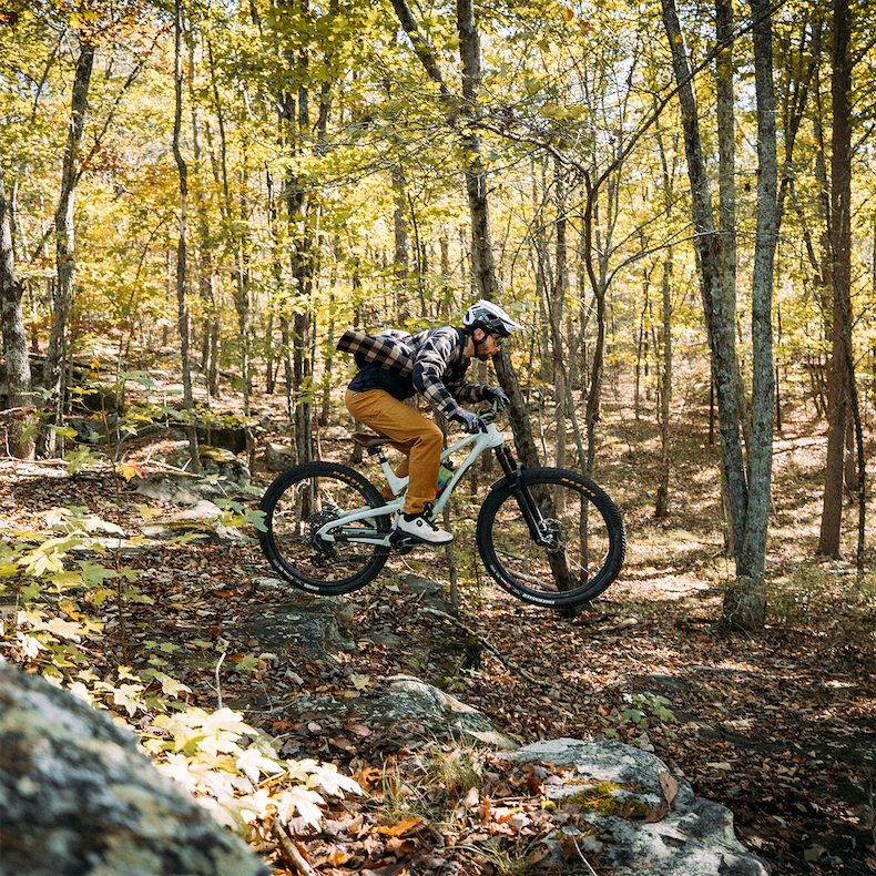 a bike rider, from a side profile, is caught flying through the air in a flannel shirt and canvas pants. 