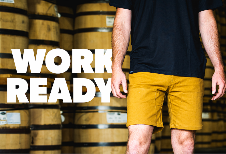 man standing in a black shirt and canvas shorts in front of barrels