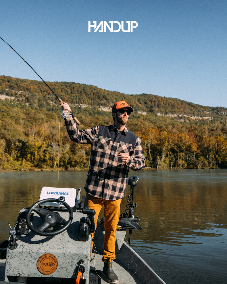 A man is fishing in a flannel that doubles as a jacket, on a fall day. 