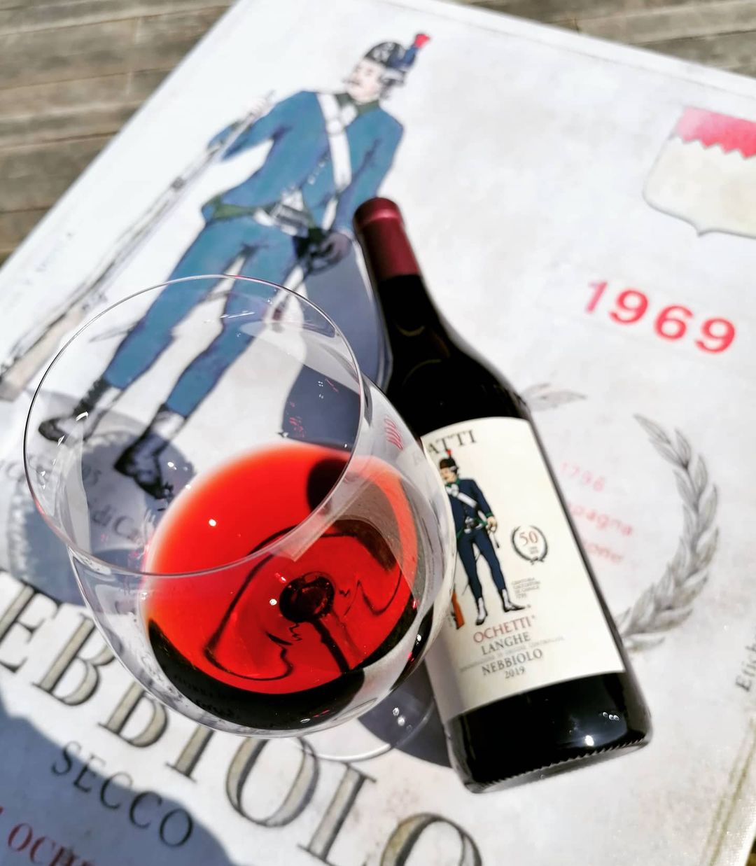 Glass and bottle of Langhe Nebbiolo Ochetti 2019 by Renato Ratti on a poster from 1969.