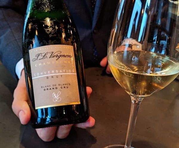 Bottle of Champagne Brut Conversation Grand Cru Blanc De Blancs by Jl Vergnon NV held in a man's hand next to a glass of champagne