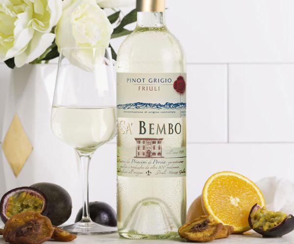 Bottle and glass of Ca Bembo Pinot Grigio Friuli Grave Doc 2020 on a table with cut lemon and cut figs.