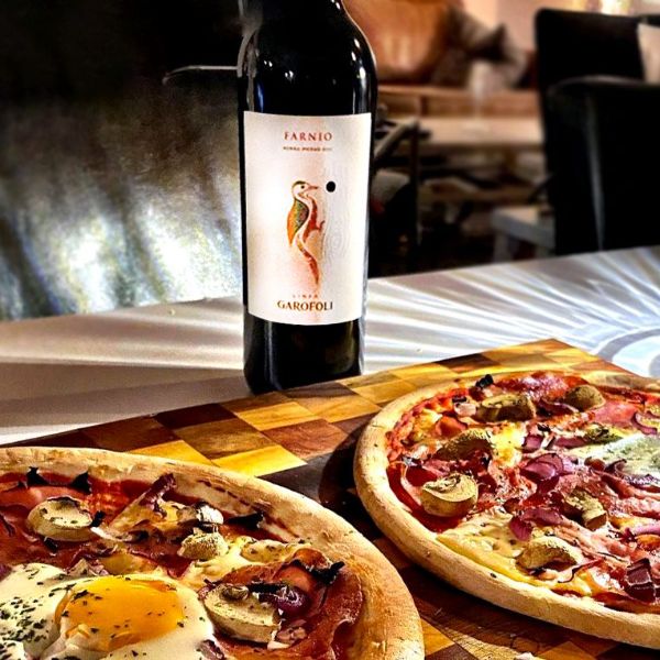 A bottle of Farnio Rosso Piceno 2020 DOC by Garofoli on a table next to two pizzas.