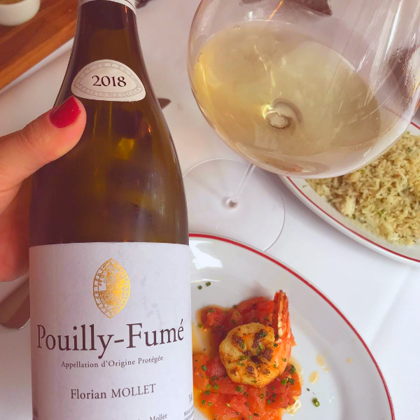 Bottle of Pouilly-Fume by Florian Mollet held up over a plate of shrimp with tomato sauce, next to a glass of white wine and a dish of rice. 