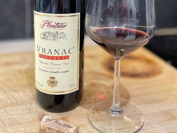 Bottle and glass of Vranac Pro Corde 2016 by Plantaze on a table with a cork.