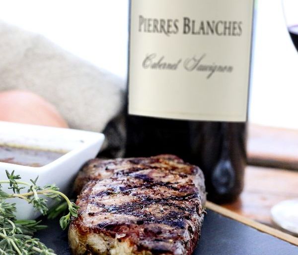 Cooked steak with hash marks in front of a bottle of Pierres Blanches Cabernet Sauvignon 2020.