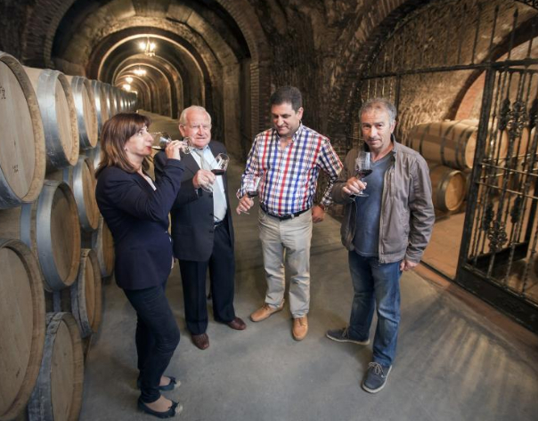 Four members of Bodegas Ismael Arroyo, producer of Valsotilla Finca Buenavista 2017 tasting wine in the cellar surrounded by oak barrels.