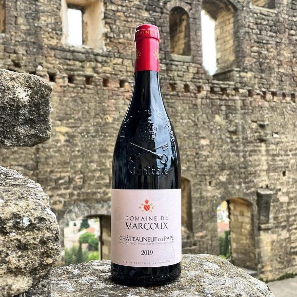 Bottle of Châteauneuf-Du-Pape 2019 by Domaine de Marcoux sitting on a rock in front of a medieval fortified stone wall.