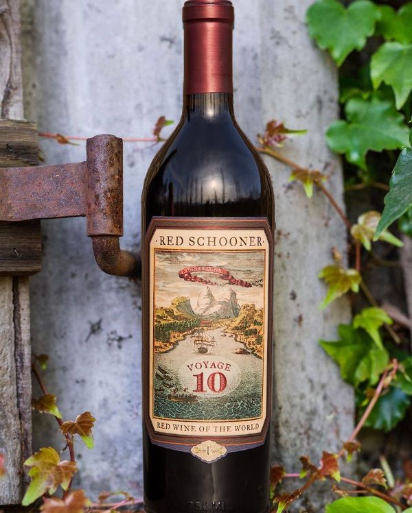 Bottle of Red Schooner Voyage 10 by Caymus Vineyards positioned in front of a wide cement gatepost.