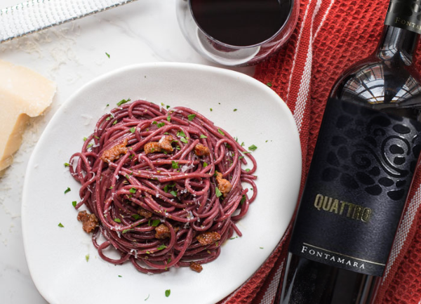 Bottle of Quattro by Fontamara 2018 next to a plate of red coloured spagetti on a white plate. Succulent visual.