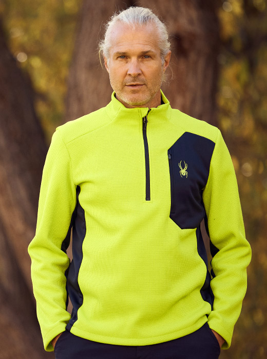 Man standing in forest wearing a lime half zip sweater