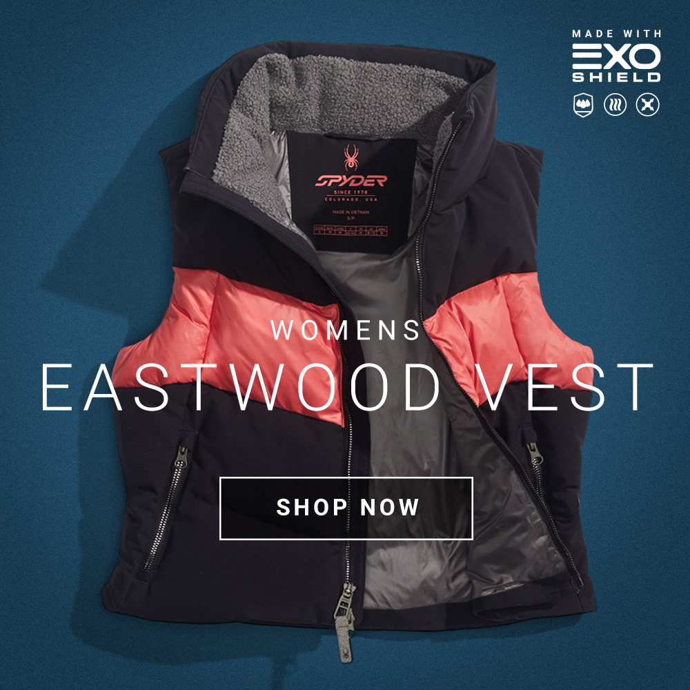 Women's Eastwood Vest by Spyder with coral color accents and gray inner lining displayed against a blue background. Text overlay says "Shop Now."