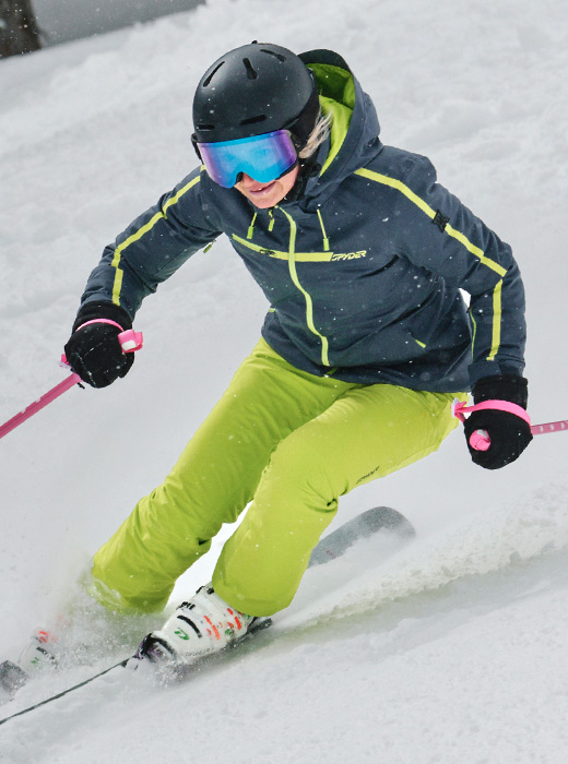 Skier in action wearing a slate blue and lime Titania jacket and lime pants