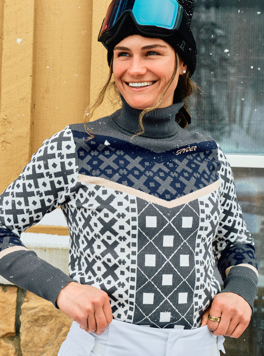 Skier standing outside with snow falling wearing a patterned ski sweater in white, grey, navy and cream.