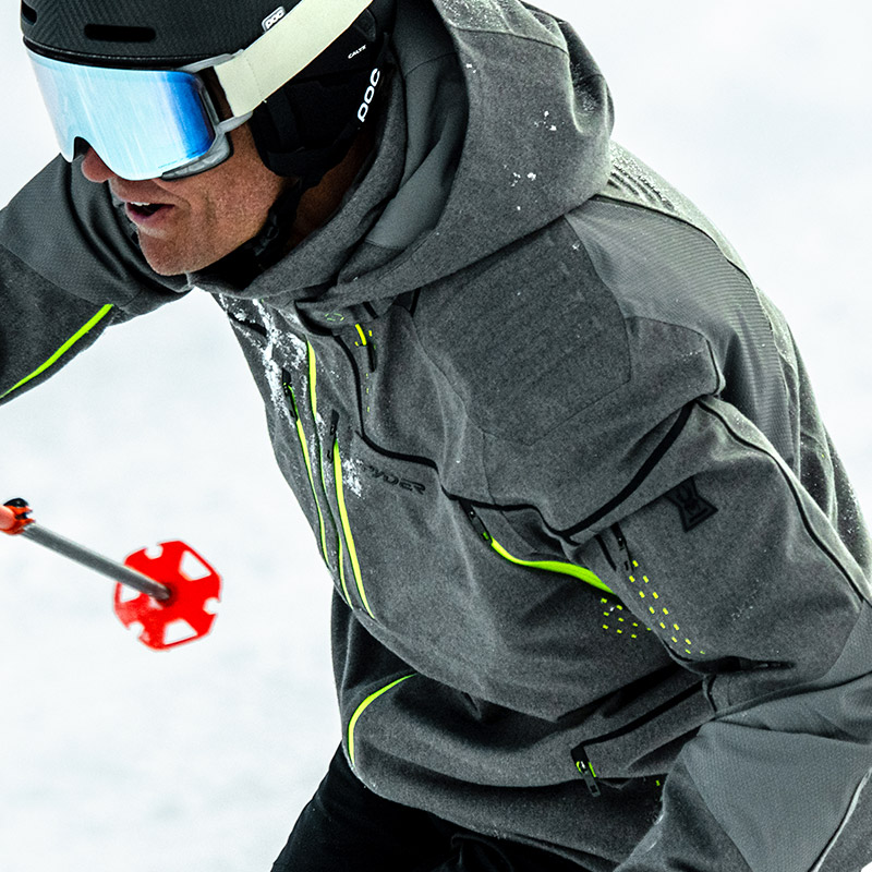 Close-up of a skier wearing a gray jacket with neon accents in a snowy background.