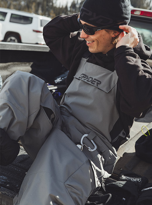 Skier sitting in the back of a trucking wearing Spyder Bib.