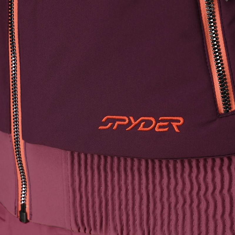 Close-up of a purple jacket with orange zippers and "Spyder" logo. The lower part features a ribbed texture, creating a sporty and sleek look.