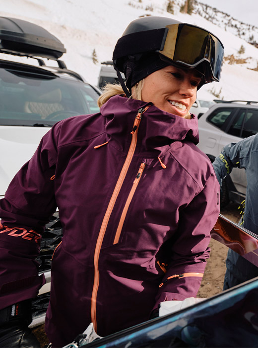 Female skier taking skis out of a pickup truck wearing a plum shell jacket.