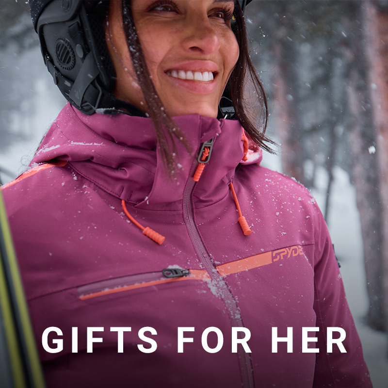 Female skier wearing a purple ski jacket in a snowy forest.  Message: Gifts for Her