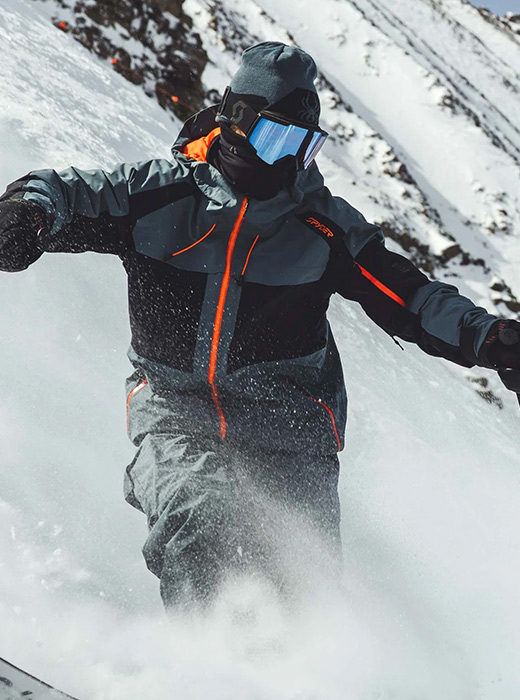 Skier coasting down a hill in a grey, black and orange ski jacket.