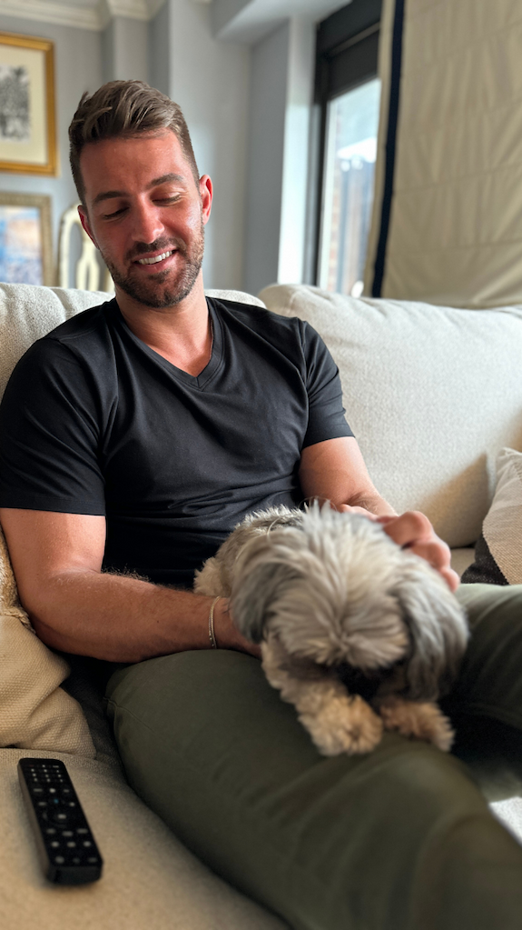 Man wearing Olive Denkhakis™ & a Black V-Neck Tee with a dog on his lap