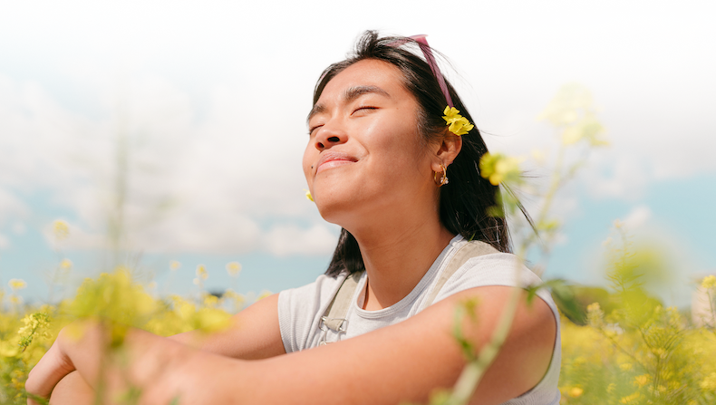 Woman sitting in a field of yellow flowers with her face towards the sun