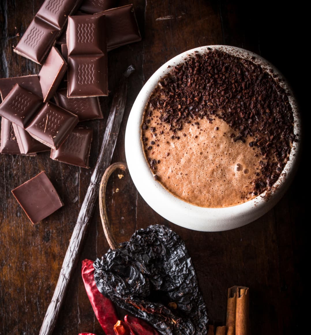 Our Mission Mocha next to a chili pepper and a pile of chocolate bar squares. 