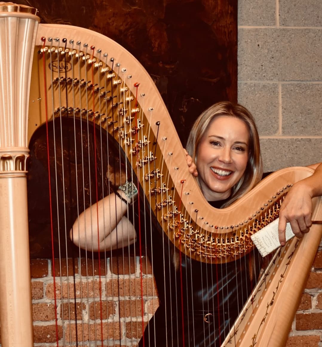 Erica Messer stands behind her harp and holds a bar of Dandelion Chocolate.