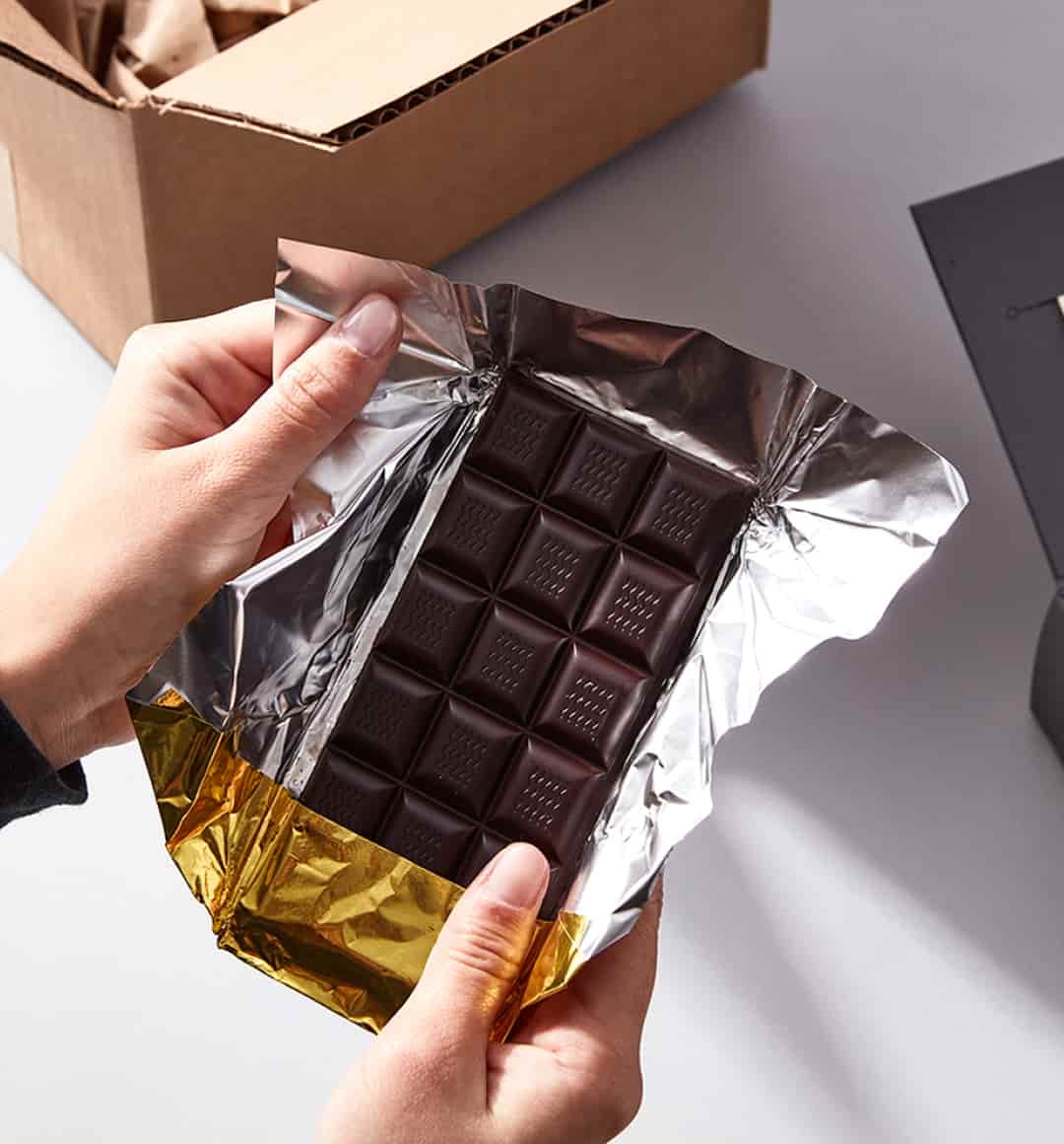 Two hands unwrap gold foil to reveal a Dandelion Chocolate bar.