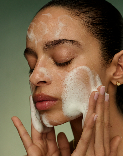 A model washing her face with the new Matcha Foam Cleanse from Tatcha, showcasing the foaming effect.