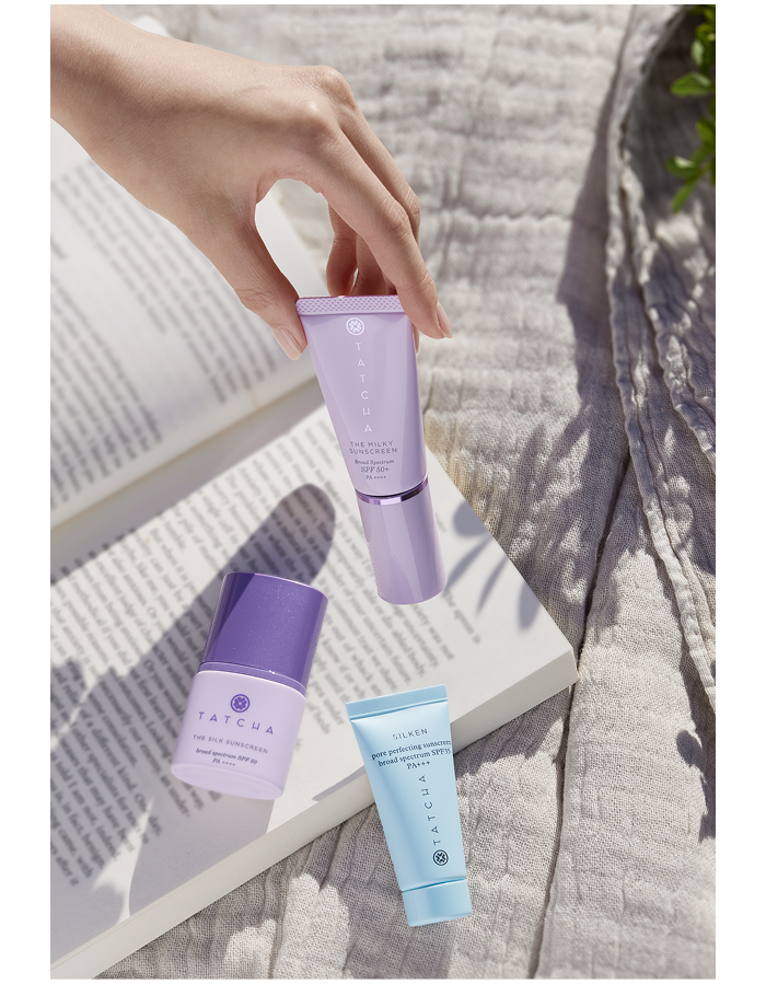 An image of Tatcha sunscreens and a book resting on a quilt 