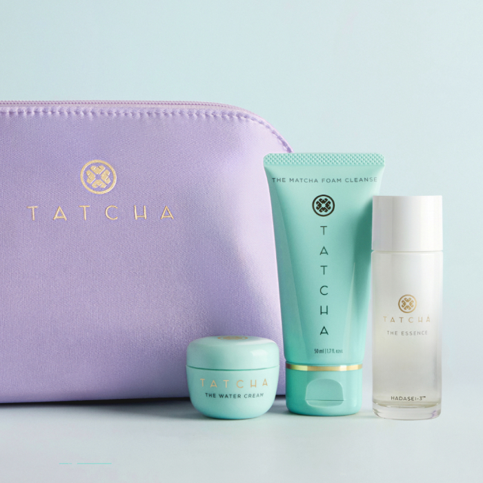 The Travel Set Curator from Tatcha: showcasing the purple travel bag, travel size Water Cream, travel size Matcha Foam Cleanse, and travel size Essence.