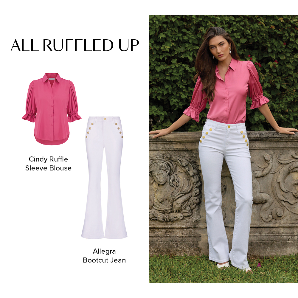 All Ruffled Up. A model is posed next to a stone ledge with a lush green hedge behind her wearing the Petal Pink Cindy Ruffle Sleeve Blouse and the White Allegra Bootcut Jean.